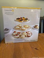 Front view of box showing image of the 3-tier ceramic serving stand with desserts on each tier and branding Celebrate It.