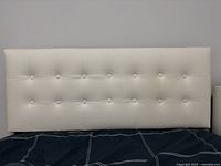 Front view of white faux leather headboard with button tufting showing the full width and height attached to bed frame.