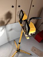 Yellow portable halogen work light with dual lamps shown on adjustable tripod stand indoors.
