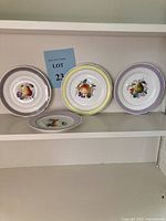 Four vintage KPM porcelain salad plates displayed on shelf showing distinct fruit designs and rim colors.