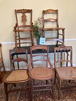 Photo showing collection of five vintage wooden chairs with cane seats arranged against a beige wall, highlighting the styles and carved details.