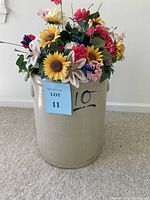 Full front view of the 10 gallon salt glaze stoneware crock with artificial flower arrangement inside. The crock has a beige glaze with distinct cobalt blue number 10 painted on the front and two side handles. It is placed on a carpeted floor against a white wall.
