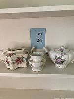 Three-piece Arthur Woods ceramic tea set on shelf including two teapots and one sugar bowl, each with floral patterns and gold rims.