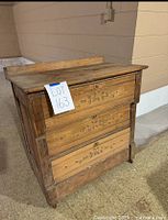 Front angled view of antique wooden chest showing three carved floral drawers, wood grain, and wear