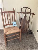 Wide shot showing antique wooden rocking chair next to vintage sled.