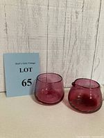 Photo showing two cranberry blown glass pieces: the creamer with twisted clear glass handle and the sugar bowl, both with subtle swirl pattern and rough pontil on bottoms.