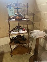 Full view of the five-tier antique walnut corner etagere and the round wooden plant stand placed next to it.