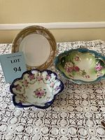 Three porcelain pieces on a lace tablecloth: large green oval bowl with pink roses, small white scalloped bowl with pink roses and navy blue trim, decorative plate with gold and tan border