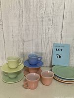 Photo of vintage Fire-King pastel glassware with teacups and saucers stacked and arranged on neutral background with a wooden textured wall.