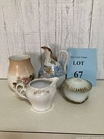 Four porcelain pieces grouped together: floral gradient vase, blue and gold pitcher, white creamer, and round trinket box