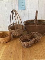 Four vintage woven baskets arranged on a wood surface with white wooden plank background. Various basket shapes and sizes are shown.