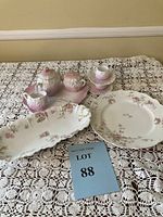 Full view of the tea set including teapot, creamer, cups with saucers, small serving tray, and two large serving plates arranged on lace tablecloth.
