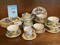 Full view of the Fratelli Fanciullacci Raffaellesco espresso set showing cups, saucers, teapot, sugar bowl, creamer, and large plate with colorful hand-painted dragon and floral motifs in yellow scalloped edging.