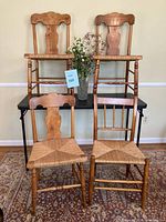 Full view of four antique wooden chairs showing two distinct back designs and rush woven seats