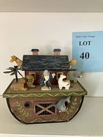 Full view of the Noah's Ark wooden music box showing the ark structure with a giraffe, lion, tree, Noah figure, zebra, elephant, and the dolphin music winder on the front side.