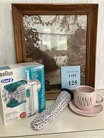 Photo showing the framed vintage photograph, Braun Oral-B electric toothbrush in box, vintage floral fabric hot water bottle, and pink 'NANA' mug with saucer arranged on a table.
