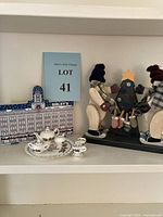 Shelf display showing three Christmas-themed items: Sibley's Cats Meow Village wooden building, porcelain Christmas tea set, and two wooden snowmen figurines with a small decorated tree.