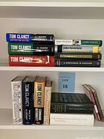 Books stacked on shelves showing Tom Clancy titles and other authors like John Feinstein, Tony Hillerman and John Updike.