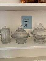 Front view of all three glass vessels on a shelf showing their size and detail with a lot sign behind them