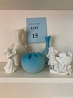Full lot showing all five items: blue satin glass rose bowl, white ceramic vase, turquoise glass bud vase, angel figurine, girl with goose figurine.