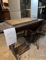 Side view of vintage Singer sewing machine table base, showing dusty wood surface, cast iron treadle and drawer detail.