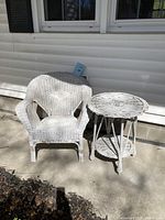 Vintage white wicker armchair and side table set positioned outdoors with visible woven texture and signs of vintage wear