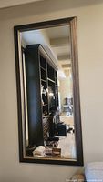 Full view of large rectangular wall mirror reflecting a room with cabinetry and furniture.