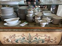 Full view showing the stash of plates, bowls, cups, teapot, gravy boat, serving platter, milk and sugar containers spread across the antique cabinet.