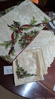 Christmas-themed ivory sateen tablecloth with festive pine and red ribbon print alongside stack of matching napkins