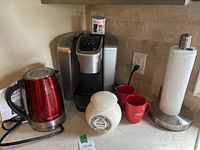 Photo of the full set: Keurig coffee maker, red Betty Crocker kettle, white ceramic sugar bowl with lid, two red Audi mugs, and chrome paper towel holder on kitchen countertop