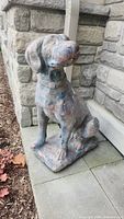 Front three-quarter view of seated concrete dog showing painted surface and base.