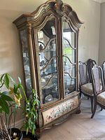 Front view of ornate display cabinet showing hand-painted detailing, glass doors, and curved top