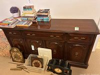 Front view of dark cherry wood dresser with books and clocks on top and around it, showing drawer and door details