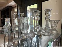Photo showing assorted clear glass candlestick holders with various faceted and ribbed designs in front of a mirror
