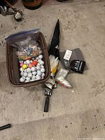 Basket filled with multi-colored golf balls and a large bag of various colored tees along with golf gloves and an umbrella beside the basket.