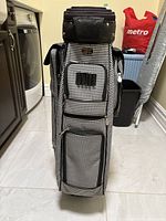 Front view of the black and white houndstooth patterned ladies golf carry bag with multiple zippered pockets and top padded section.