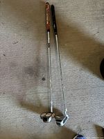 Two right-handed golf putters on a carpeted floor showing the full length including putter heads and shafts