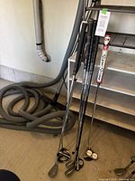 Four left-handed golf clubs leaning against a wall on a garage floor including irons and putters with distinct grips.