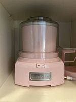 Front view of the pink Cuisinart ice cream maker showing the base unit with on/off switch and clear lid on top.