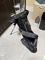 Full view of black and gray US Kids Golf junior golf bag with stand, showing clubs inside and padded shoulder straps.