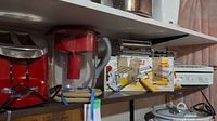 Shelf view showing red toaster, Brita water jug, Marcato Multipart pasta maker box, ravioli pans and other kitchen items