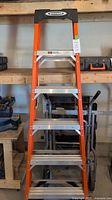 Full front view showing orange fiberglass rails, black top cap, aluminum steps on workshop shelf.