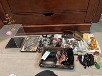 Overview of trays with necklaces, bracelets, sunglasses, watches and display items on floor in front of wooden cabinet