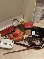 Photo of assorted ladies leather purses, bags, and belts in various colors arranged on the floor including brown handbag, red clutches, and belts.