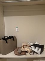 Four ladies bags and purses on a shelf, including O bag tote, small beige purse, and polka-dot purses.