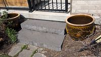 Wide shot showing two large brown glazed planters placed outdoors on ground near patio steps.