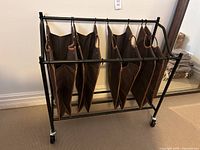 Side view of black metal laundry hamper featuring four brown hanging fabric bags and castor wheels.