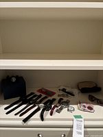 White shelf with blue box and below assorted watches, strap kits, sunglasses, currency, key ring; lot tag visible