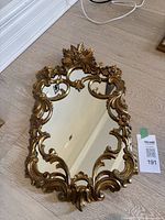 Full view of small gold ornate mirror showing overall shape and condition on floor surface