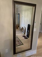 Full view of large wall mirror mounted on beige wall, showing the rectangular shape and light brown frame with metallic trim.